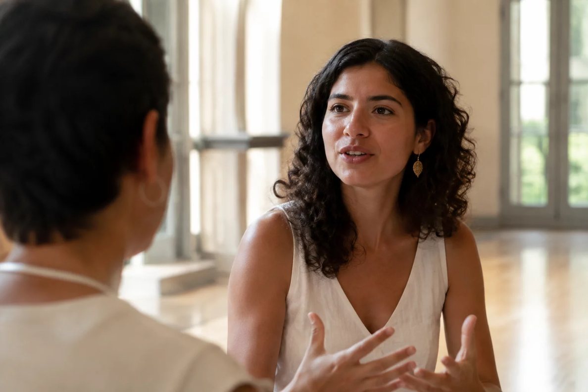Duas pessoas sentadas de frente uma para a outra à mesa: uma fala, a outra registra por escrito